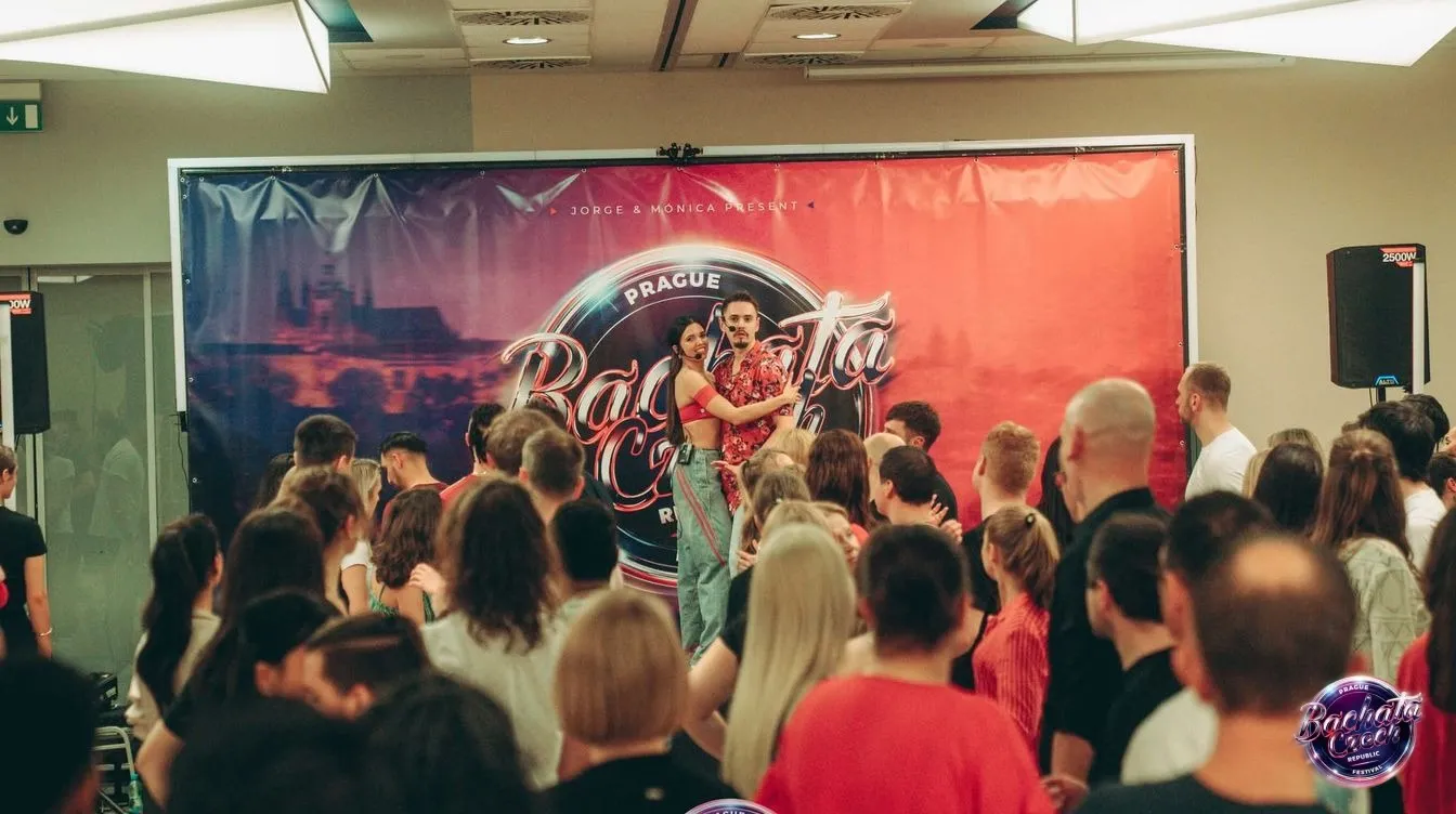 Dancers in front of the Bachata Czech Republic Festival banner watching an artist couple